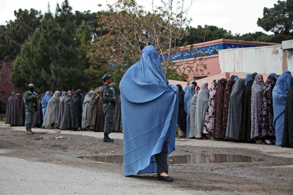 An Afghan burqa-clad woman walks by people lining up for the voting registration before they cast their ballots at a polling station in Herat, Afghanistan, Saturday, April 5, 2014. Afghan voters lined up for blocks at polling stations nationwide on Saturday, defying a threat of violence by the Taliban to cast ballots in what promises to be the nation's first democratic transfer of power. (AP Photo/Hoshang Hashimi)