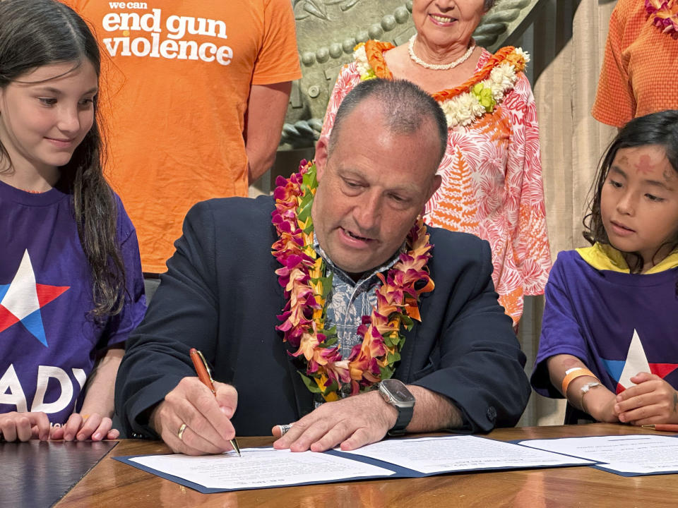 Hawaii Gov. Josh Green signs gun control legislation in Honolulu on Friday, June 2, 2023 as Leia Kandell, left, age 10, and Cole Kandell, age 7, look on. Green signed legislation that allows more people to carry concealed firearms but at the same time prohibit people from taking guns to a wide range of places, including beaches, hospitals, stadiums, bars that serve alcohol and movie theaters. (AP Photo/Audrey McAvoy)