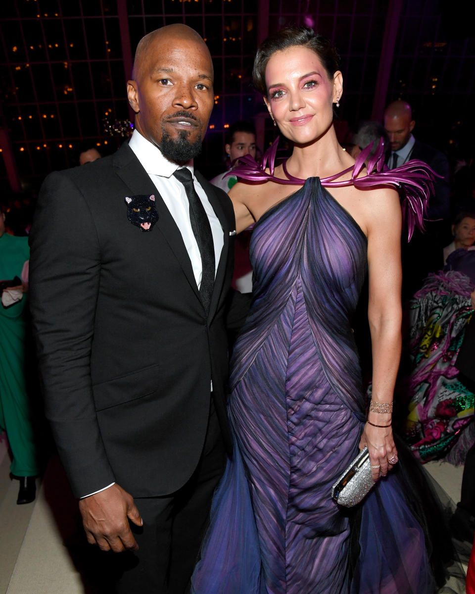 Jamie Foxx and Katie Holmes pose together; Holmes wears a purple pleated gown with ribbon details