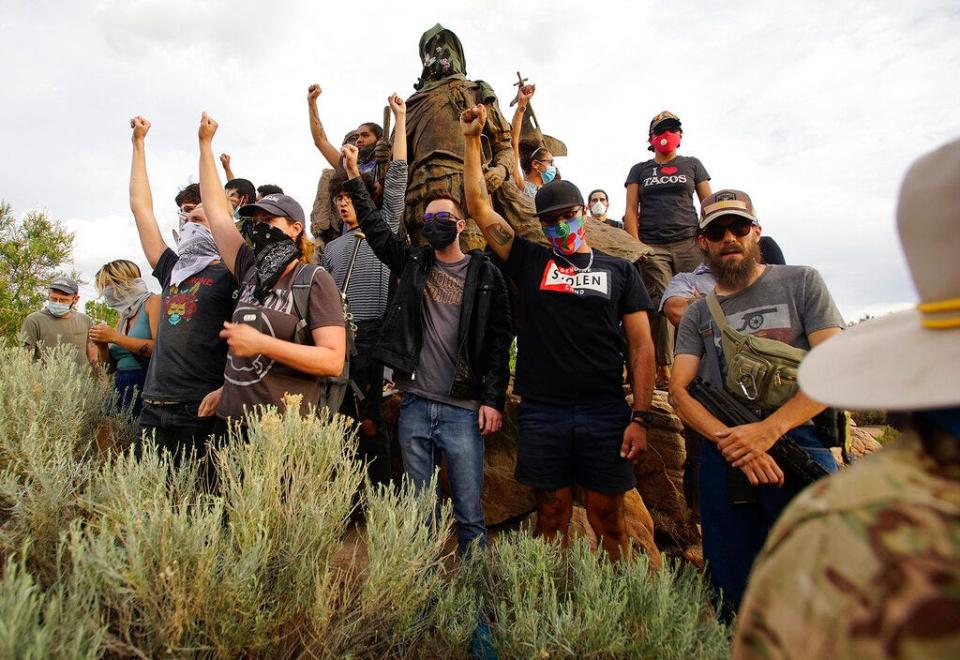 Demonstrators climb the statue of Don Juan de Oñate in Old Town in Albuquerque, N.M., while an armed member of the New Mexico Civil Guard stands by during a protest calling for the removal of the likeness of the controversial New Mexico explorer Monday, June 15, 2020.