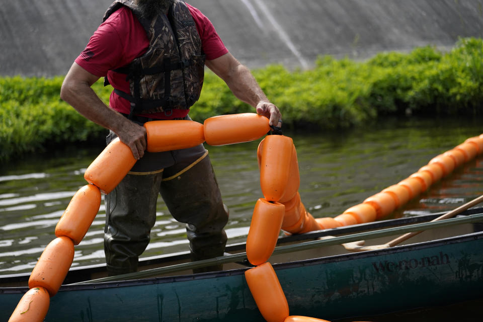 Employees of Osprey Initiative lays boom as they install a Litter Gitter, to help collect trash at the source before it travels into larger bodies of water, in Metairie, La., Thursday, May 19, 2022. Many novel devices are being used or tested worldwide to trap plastic trash in rivers and smaller streams before it can get into the ocean. (AP Photo/Gerald Herbert)