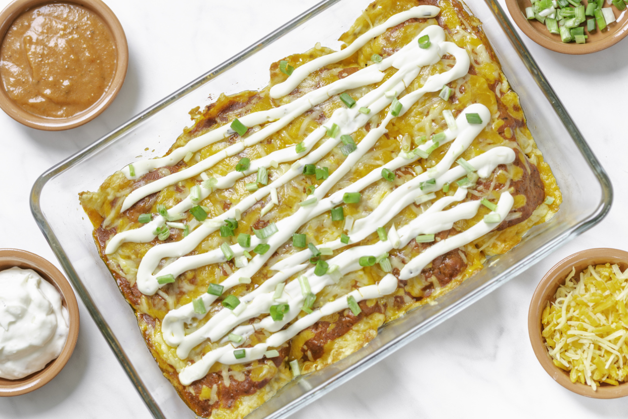 Mexican food, homemade beef ground enchiladas in a ketogenic style with cheese tortillas in a glass oven dish on a white background with ingredients - directly above view