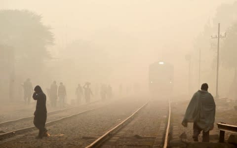 Pakistani residents walk alongside the railway track on a foggy day in Lahore  - Credit: AFP