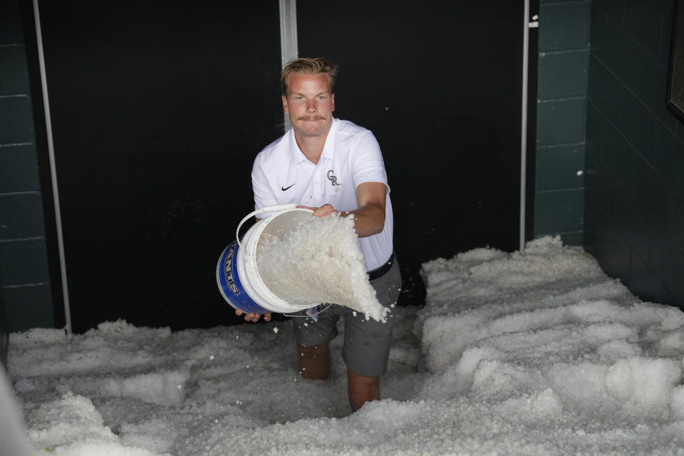 Clubhouse attendant Csey Williams uses a bucket to bail a mixture of water and hail out from in front of the clubhouse doors of the home dugout after a summer storm Thursday, June 29, 2023, in Denver. The Colorado Rockies were scheduled to play against the Los Angeles Dodgers. (AP Photo/David Zalubowski)
