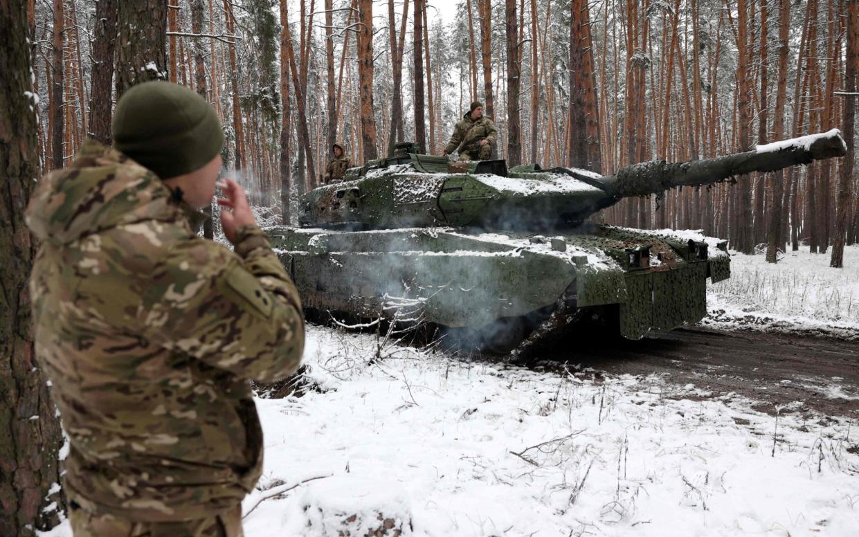 A Ukrainian soldier smokes as a snow-covered Leopard 2 tank passes by in Donetsk