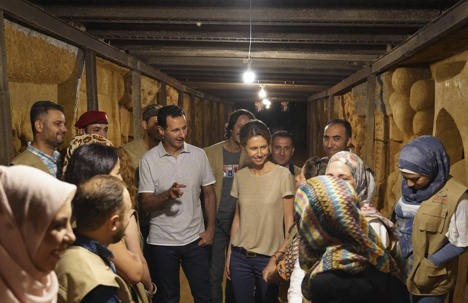 FILE - In this Aug. 16, 2018, file photo, released on the official Facebook page of the Syrian Presidency, Syrian President Bashar Assad, center left, and his wife Asma, center right, talk with Syrian artists during their visit to one of tunnels that were dug by rebels while they were under siege, in Jobar, near the Syrian capital Damascus, Syria. The unprecedented public crackdown on Syria's wealthiest businessman Rami Makhlouf,, a close cousin of Bashar Assad, comes as the embattled president seeks to consolidate power and rein in war profiteers. Syria is preparing for a new phase of economic hardship and U.S.-led sanctions that some say might be more difficult to weather than war. (Syrian Presidency Facebook Page via AP, File)