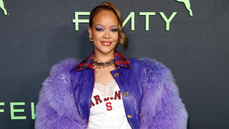 Rihanna wearing a purple feathered coat with a varstiy-style tee and colorful jeweled necklaces