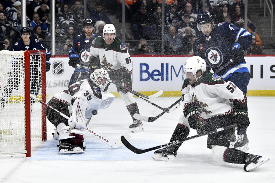 Arizona Coyotes goaltender Connor Ingram (39) makes a save as Coyotes' Sean Durzi (50) and Winnipeg Jets defenseman Neal Pionk (4) looks for a rebound during the second period of an NHL hockey game in Winnipeg, Manitoba on Sunday, Feb. 25, 2024. (Fred Greenslade/The Canadian Press via AP)