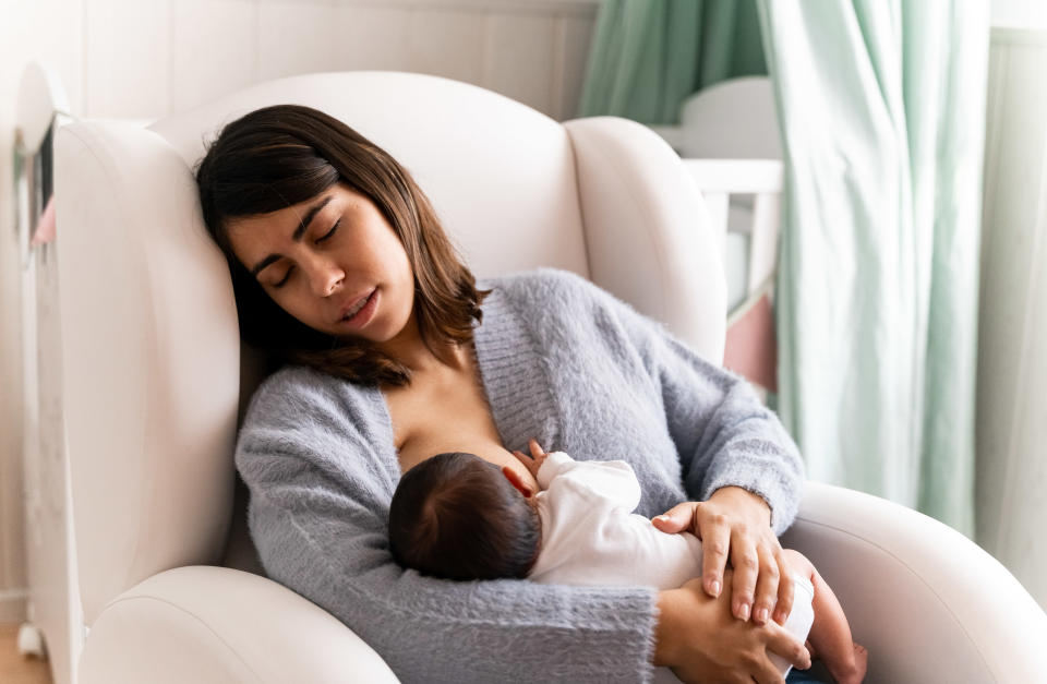 Exhausted mother sitting on nursing chair while breastfeeding her baby. Exhaustion of mothers due to lack of sleep is normal in the first months of a baby's life.