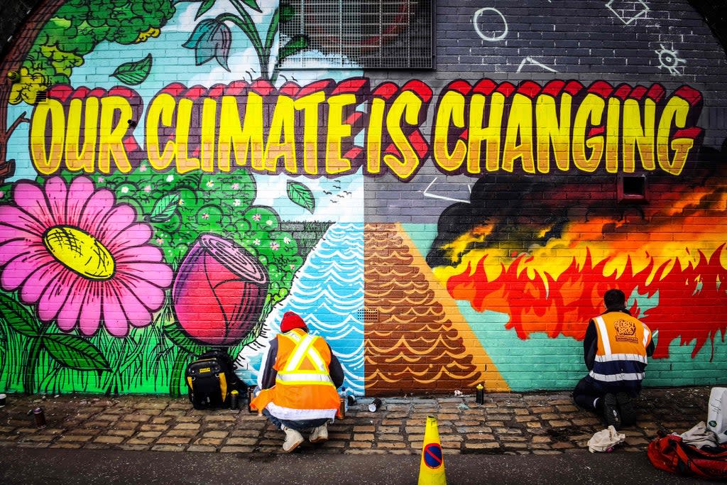 Street artists paint a mural on a wall opposite the Cop26 climate summit venue in Glasgow (AFP via Getty Images)