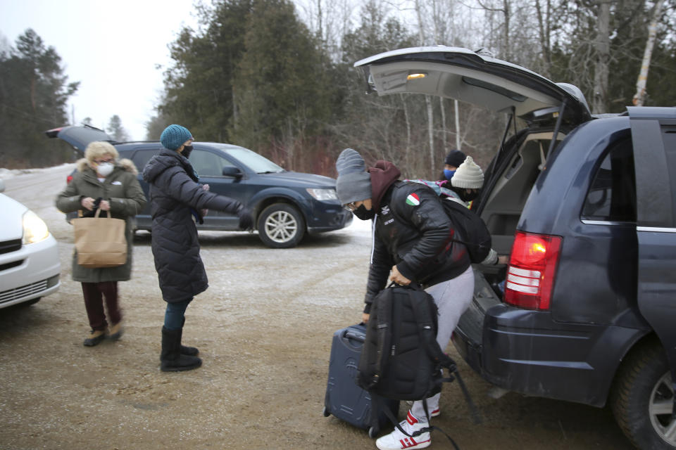 Migrants, right, remove their luggage from a taxi, in Champlain, N.Y., as they prepare to cross the Canadian border to arrive at a reception center for irregular borders crossers, less than 100 feet (about 30 meters) away, in Saint-Bernard-de-Lacolle, Quebec, in Canada, Wednesday Jan. 12, 2022. The refugees are crossing the U.S.-Canadian border where they are arrested by the Royal Canadian Police in Saint-Bernard-de-Lacolle, Quebec, and then allowed to make asylum claims and remain in Canada while those claims are processed. The process was halted for most cases after the 2020 outbreak of COVID-19, but the Canadian government changed its policy in November, allowing the process to continue. (AP Photo/Wilson Ring)