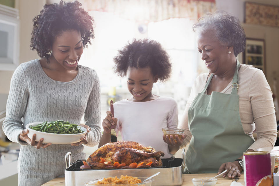 small group of people gathering around a turkey in a roasting pan