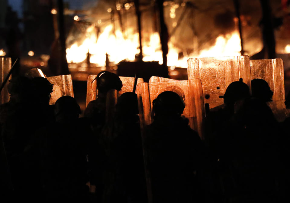 Policías antimotines miran las llamas de varias carpas levantadas por manifestantes contrarios al gobierno, a las que prendieron fuego hombres vestidos de civil que se cree eran una unidad privada de guardias parlamentarios, durante protestas en Beirut, Líbano, el sábado 18 de enero de 2020. (AP Foto/Hussein Malla)