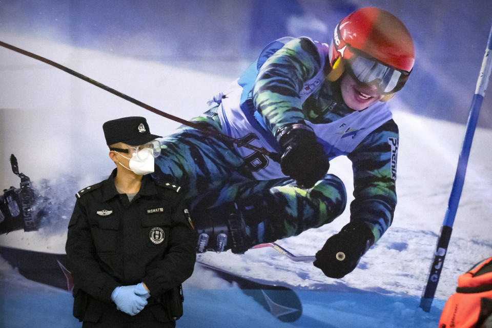 FILE - A police officer wearing a face mask and goggles to protect against COVID-19, stands near a poster of a skier on the wall at a train station in Zhangjiakou in northern China's Hebei Province, Friday, Nov. 26, 2021. China is threatening to take “firm countermeasures" if the U.S. proceeds with a diplomatic boycott of February's Beijing Winter Olympic Games. Foreign Ministry spokesperson Zhao Lijian on Monday accused U.S. politicians of grandstanding over the issue of not sending dignitaries to attend the events that China hopes will showcase its economic development. (AP Photo/Mark Schiefelbein, File)