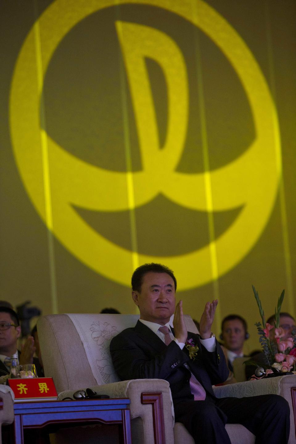 Wanda Chairman Wang Jianlin applauds in front of the logo for Dalian Wanda Group during an event at a hotel in Beijing, China, Wednesday, June 19, 2013. Chinese property and cinema conglomerate Dalian Wanda Group said it is buying British yacht maker Sunseeker and will develop an upmarket London hotel, expanding into the luxury market as part of the latest foray abroad by a major Chinese firm. (AP Photo/Ng Han Guan)