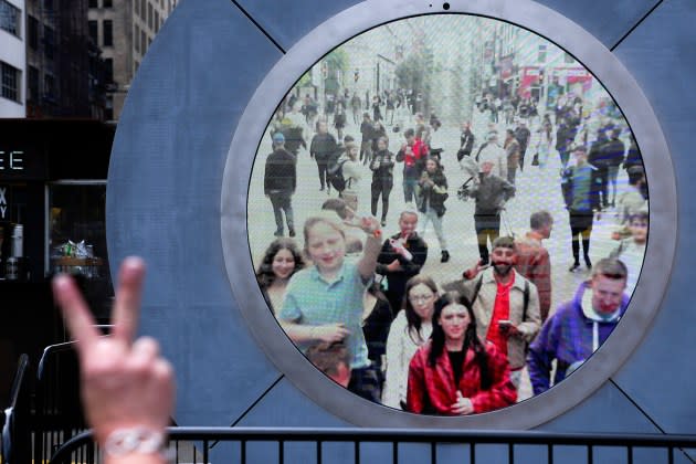 People in both New York and Dublin, Ireland, wave and signal at each other while looking at a livestream view of one another as part of an art installation on the street in New York, Tuesday, May 14, 2024.  - Credit: Seth Wenig/AP