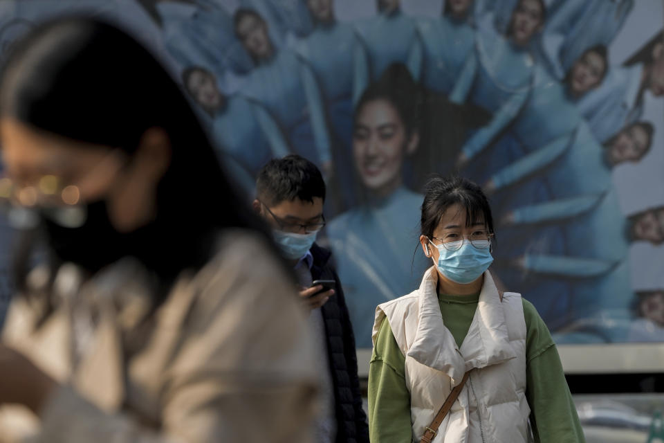 People wearing face masks walk by an advertisement billboard on street in Beijing, Wednesday, Nov. 2, 2022. (AP Photo/Andy Wong)