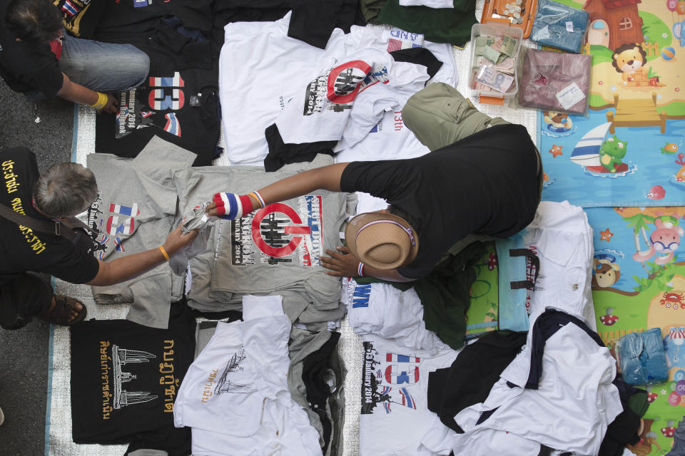 A merchant hands a t-shirt to a potential customer near an anti-government People's Democratic Reform Committee (PDRC) protest camp in the Pathumwan district, Wednesday, Jan. 15, 2014, in Bangkok, Thailand. Gunshots rang out in the heart of Thailand's capital overnight in an apparent attack on anti-government protesters early Wednesday that wounded at least two people and ratcheted up tensions in Thailand's deepening political crisis. (AP Photo/John Minchillo)