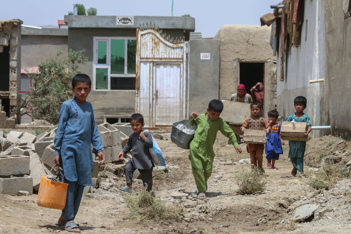 Afghan children carry their belongings following flash floods in the Khair Abad area in Ghazni province (AFP via Getty Images)