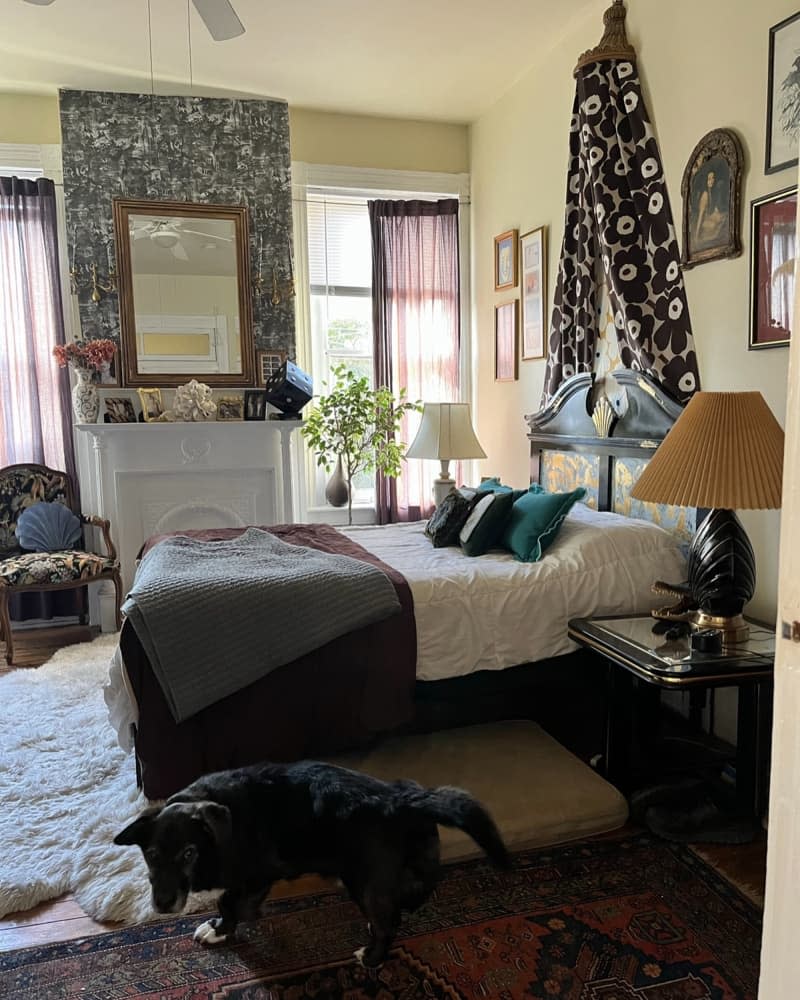 Wallpaper behind wall mirror accents white mantel in bedroom with pale yellow walls.