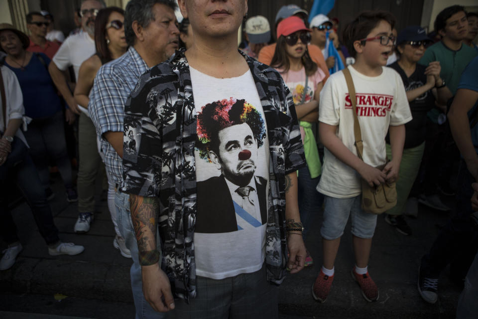 A man wears a t-shirt with a cartoon of Guatemalan President Jimmy Morales as a clown during a protest against the government organized by civil society groups in front of the Presidential House in Guatemala City, Saturday, July 27, 2019. (AP Photo/ Oliver de Ros)