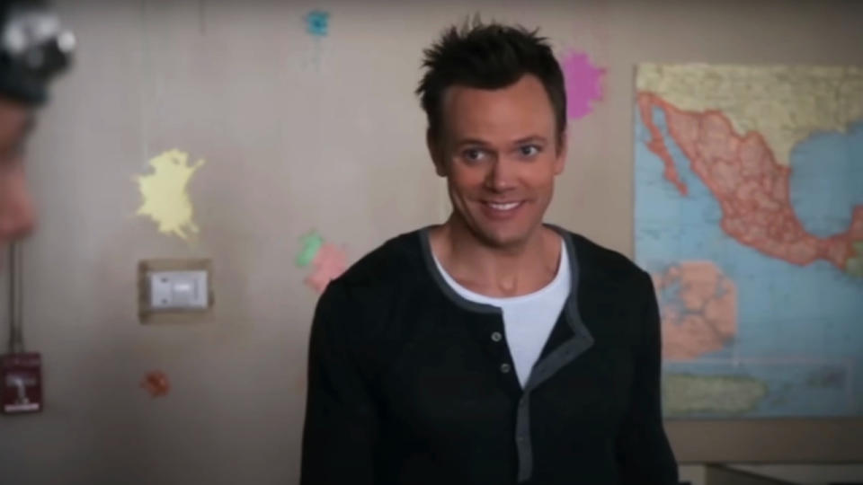 Joel McHale smiles in disbelief in a paint splattered classroom in Community.