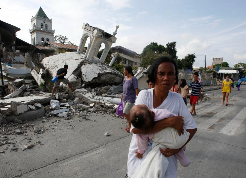 FILE PHOTO: A woman carries her baby past a destroyed church belfry in Tubigon, Bohol, a day after an earthquake hit central Philippines October 16, 2013. (Source: REUTERS/Erik De Castro)