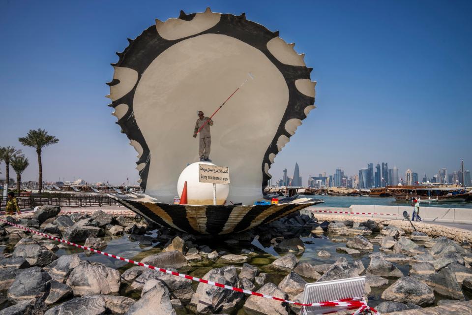 A migrant laborer paints The Pearl Monument, a sculpture depicting an open oyster shell with running water, on the corniche, overlooking the skyline of Doha, Qatar, Wednesday, Oct. 19, 2022.