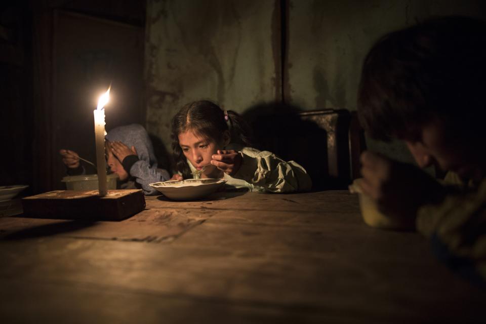 FILE - In this Monday, June 8, 2020 file photo Siblings Estiben Aquiño, 4, Estefany Aquino, 11, and Javier Aquino, 14, eat dinner illuminated by a candle in their home in the Nueva Esperanza neighborhood that has no access to electricity, in Lima, Peru. (AP Photo/Rodrigo Abd, File)