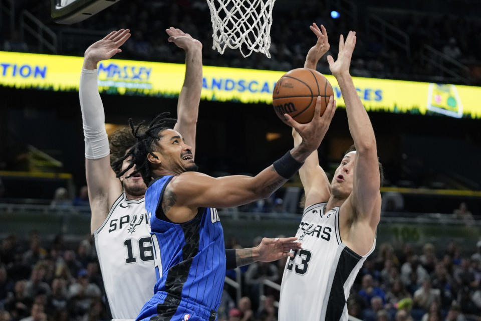 Orlando Magic guard Gary Harris, center, gets between San Antonio Spurs forwards Cedi Osman (16) and Zach Collins (23) to shoot during the first half of an NBA basketball game, Thursday, Feb. 8, 2024, in Orlando, Fla. (AP Photo/John Raoux)