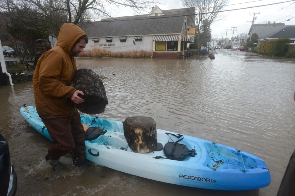 Dylan Kaeselau retrieves his scattered firewood with a kayak after his Bradford Street home was severely flooded on Dec. 23 in the east end of Provincetown. The East End Market, owned by Oriana Conklin, is in the background.