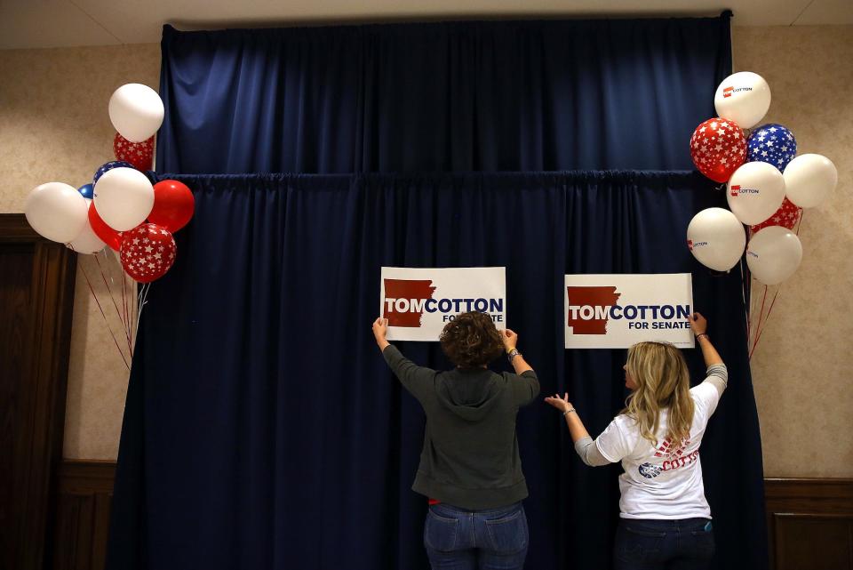 Two campaign staffers try to figure out where to hang "Tom Cotton for Senate" signs on a dark blue curtain adorned with red, white, and blue balloons on each side ahead of an election night gathering in Little Rock, Arkansas.