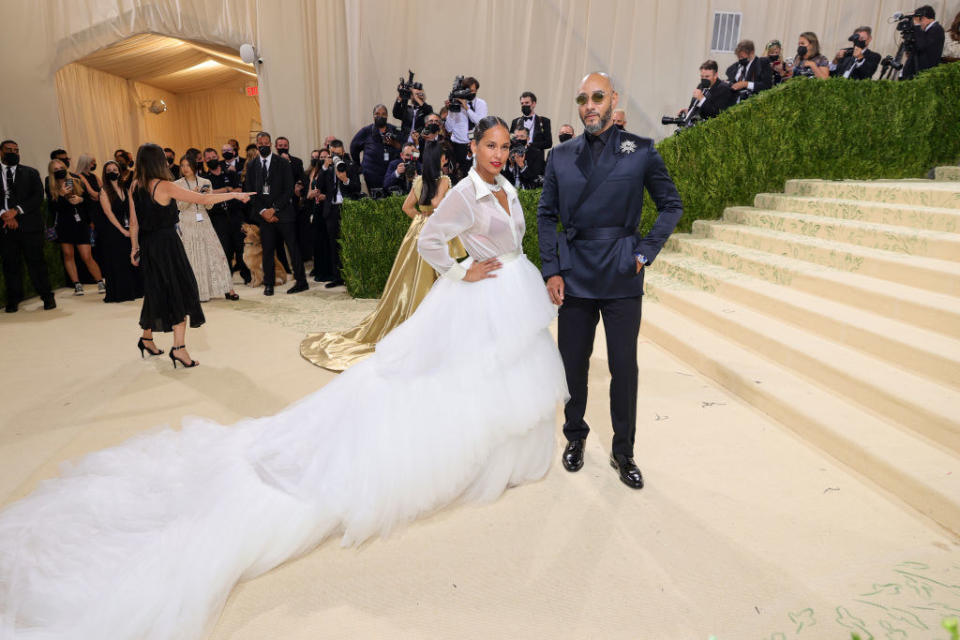 Alicia Keys wears a long sleeve collared gown with a long, ruffle train and Swizz Beatz wears a dark colored suit with a flower on his lapel