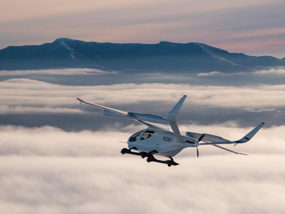 A while Beta Technologies CX300 flying over clouds.