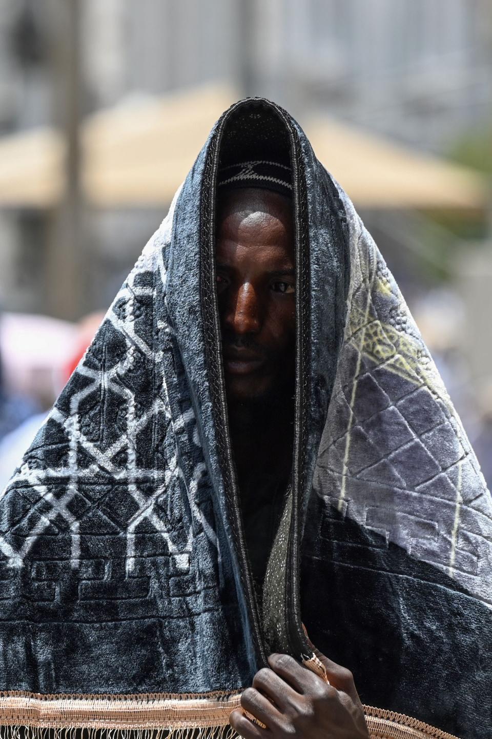 A Muslim pilgrim uses a prayer mat to protect himself from the sun as he walks in the holy city of Mecca on June 23, 2023, as Muslims from around the world arrive for the annual Hajj pilgrimage.