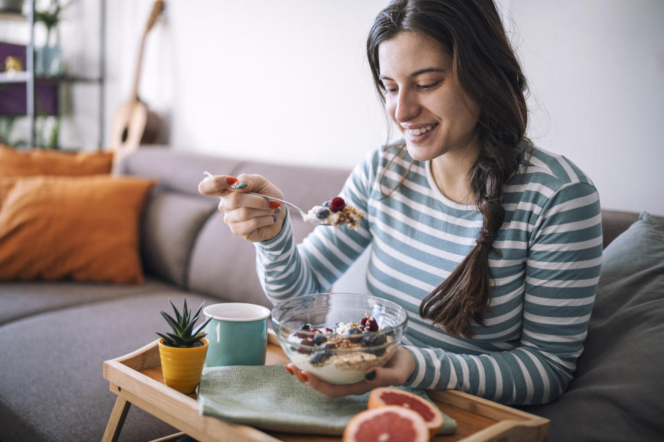 Smiling woman having breakfast in the morning at home, yogurt and berries