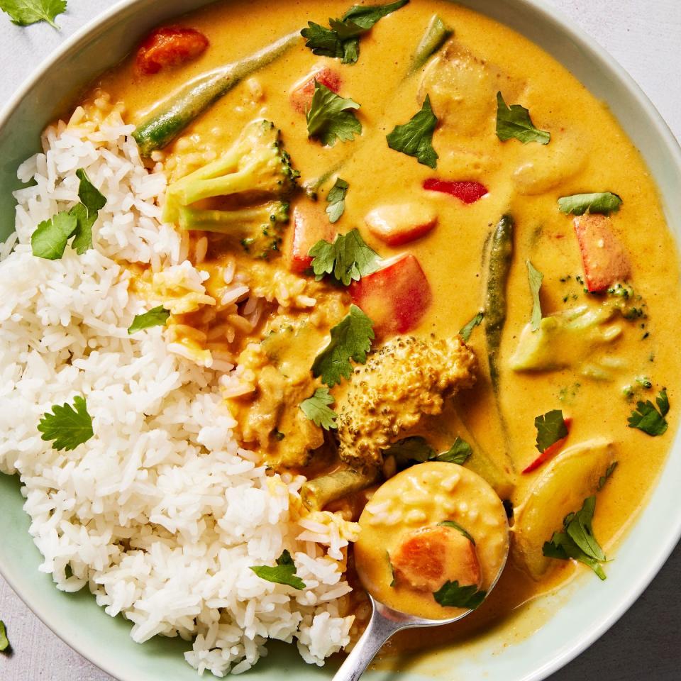 a bowl of rice with a coconut milk based curry sauce, broccoli, green beans, carrots, potatoes and bell peppers