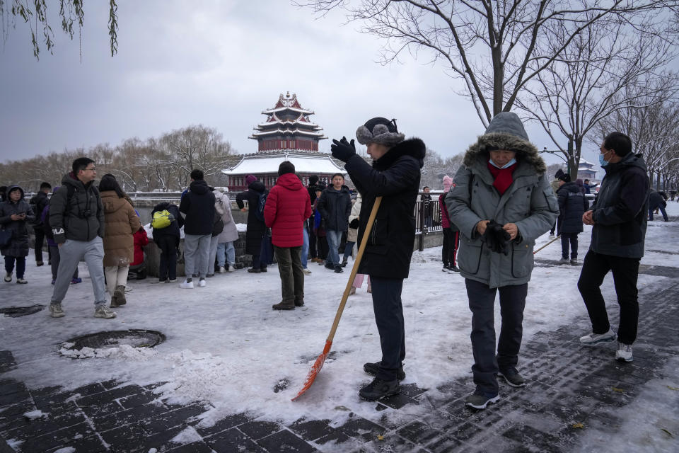 City workers clear the snow on a pathway as people take pictures of the snow covered Turret of the Forbidden City in Beijing, Monday, Dec. 11, 2023. An overnight snowfall across much of northern China prompted road closures and the suspension of classes and train service on Monday. (AP Photo/Andy Wong)
