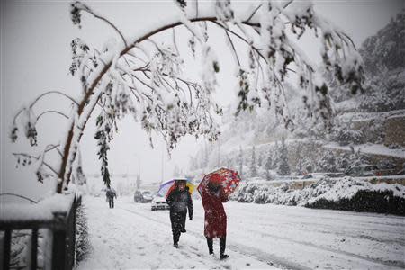 Women walk with umbrellas on a snow-covered road during winter in Jerusalem December 12, 2013. REUTERS/Amir Cohen