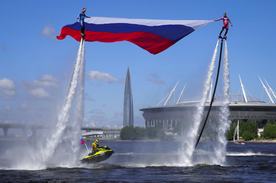 Members of the Russian hydroflight team hold the Russian national flag during the Day of Russia celebration in St.Petersburg, Russia, Friday, June 12, 2020, with business tower Lakhta Centre, the headquarters of Russian gas monopoly Gazprom and Gazprom Arena soccer stadium in the background. (AP Photo/Dmitri Lovetsky)