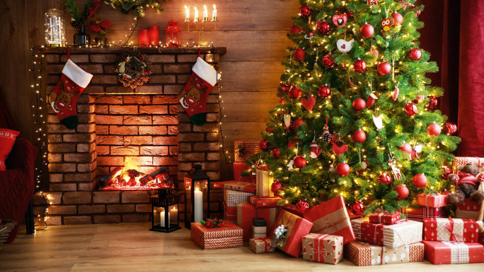 A decorated Christmas tree with presents beneath next to a fireplace