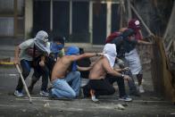 Imagen del sábado 22 de febrero de 2014 que muestra a manifestantes opositores al gobierno resguardándose de la policía antidisturbios en Caracas, Venezuela. Tras el mitin opositores algunas personas levantaron barricadas con basura y desechos y lanzaron piedras y botellas contra la Policía y la Guardia Nacional. (Foto de AP/Rodrigo Abd)