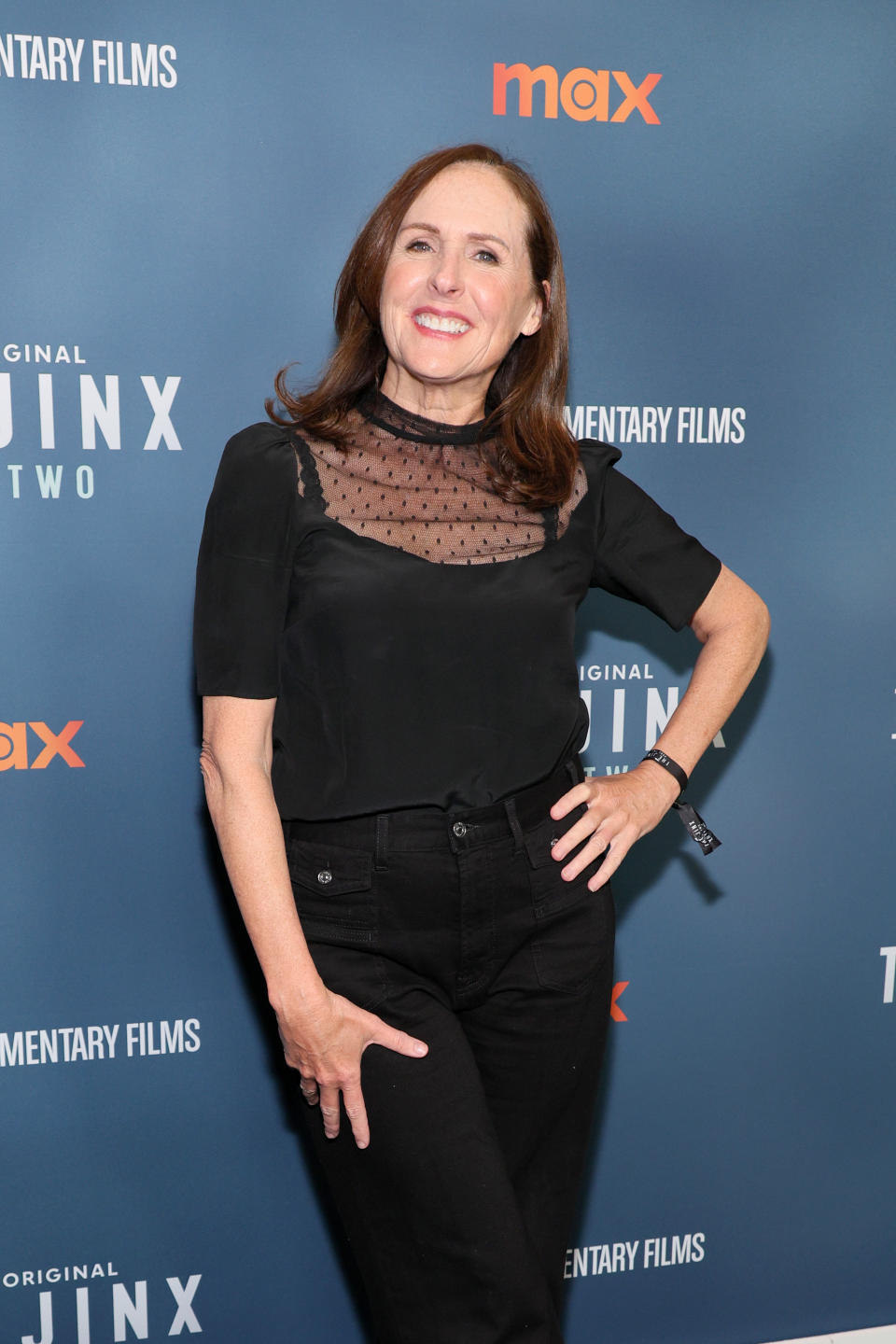 Molly Shannon posing on the red carpet, wearing a sheer black top and black pants, at an event for Max Original's documentary films