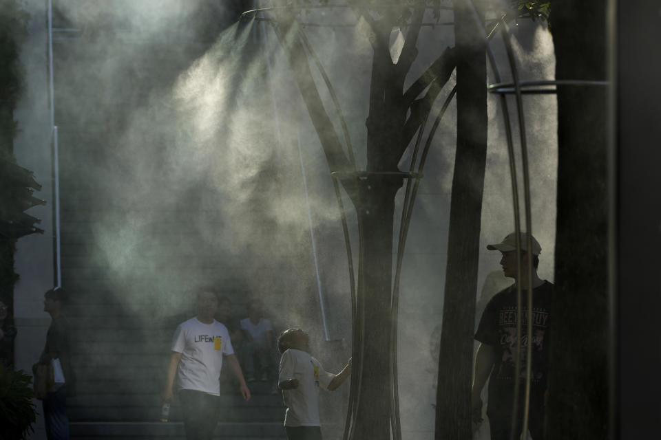 Visitors to a mall cool off near a mist machine during the summer heat in Beijing, Saturday, June 15, 2024. (AP Photo/Ng Han Guan)