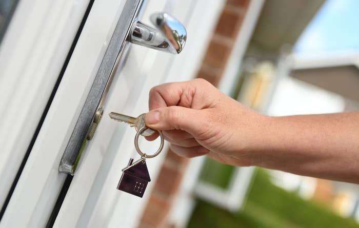 A hand inserting a key into a door lock, with a house-shaped keychain attached to the key ring