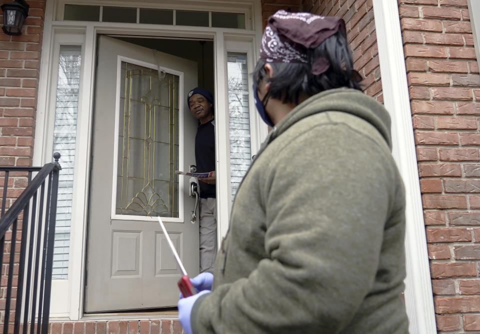 Graco Hernandez Valenzuela speaks to voter Tyrone Vereen, at door, while canvassing the area for the Working Families Party regarding the U.S. Senate races, Wednesday, Dec. 16, 2020, in Lawrenceville, Ga. Vereen, who had already mailed in his ballot a week prior, said the events of the last year convinced him it was “time for a change.” (AP Photo/Tami Chappell)