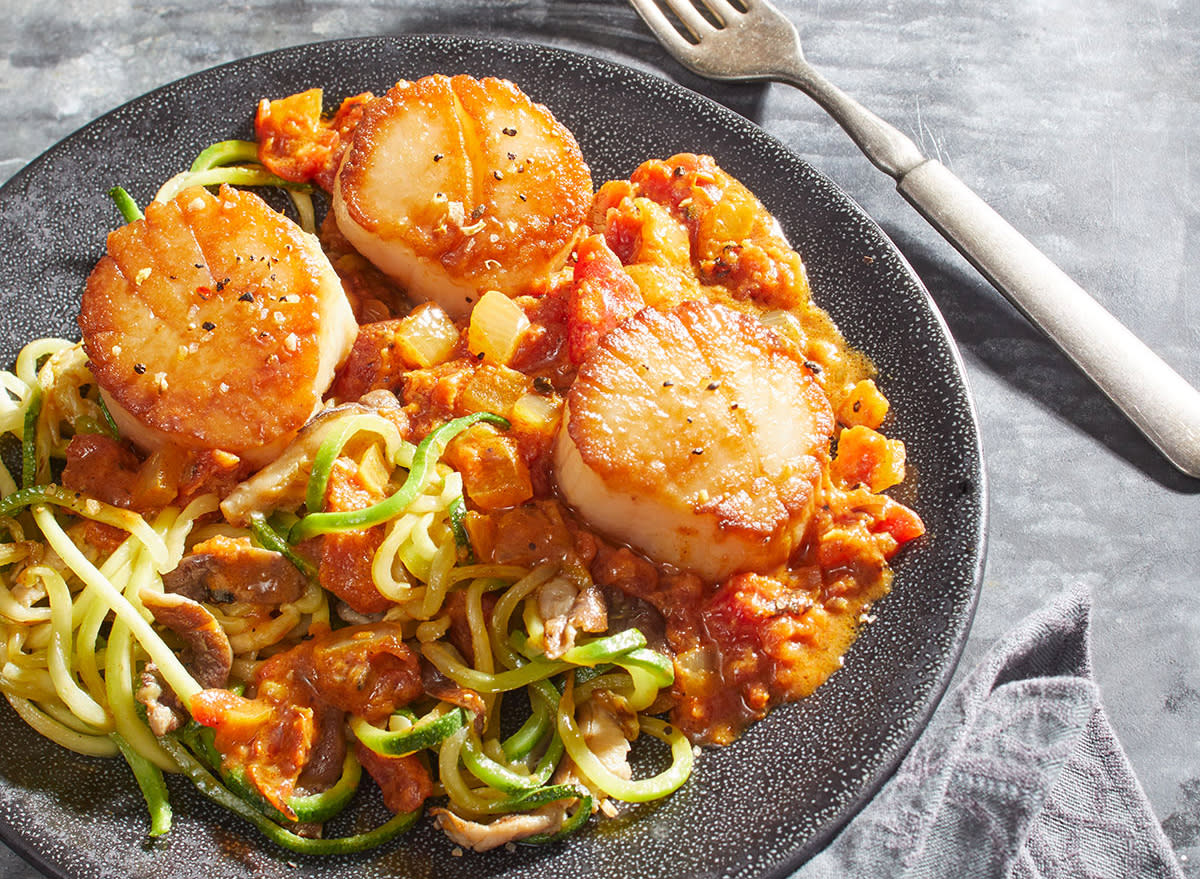 keto thai curry with scallops, zucchini noodles, and shiitake mushrooms on a gray plate with fork