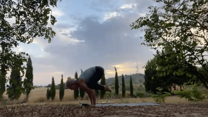 Woman practicing an arm balance outside at sunrise on her yoga mat