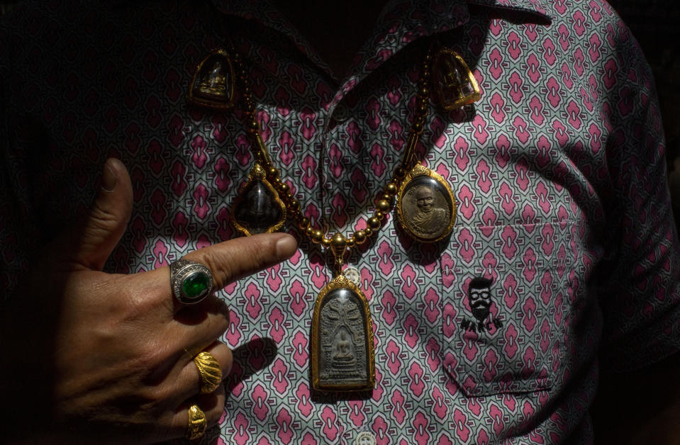 An amulet seller points to what he is wearing at a market in Bangkok, Thailand, Tuesday, June 2, 2020. Amulet markets were allowed to reopen on Monday, June 1, 2020 as the Thai government continues to ease restrictions related to running business in the capital Bangkok that were imposed weeks ago to combat the spread of COVID-19. Believers in amulets say they can bring good fortune, true love or just about anything else. (AP Photo/ Gemunu Amarasinghe)