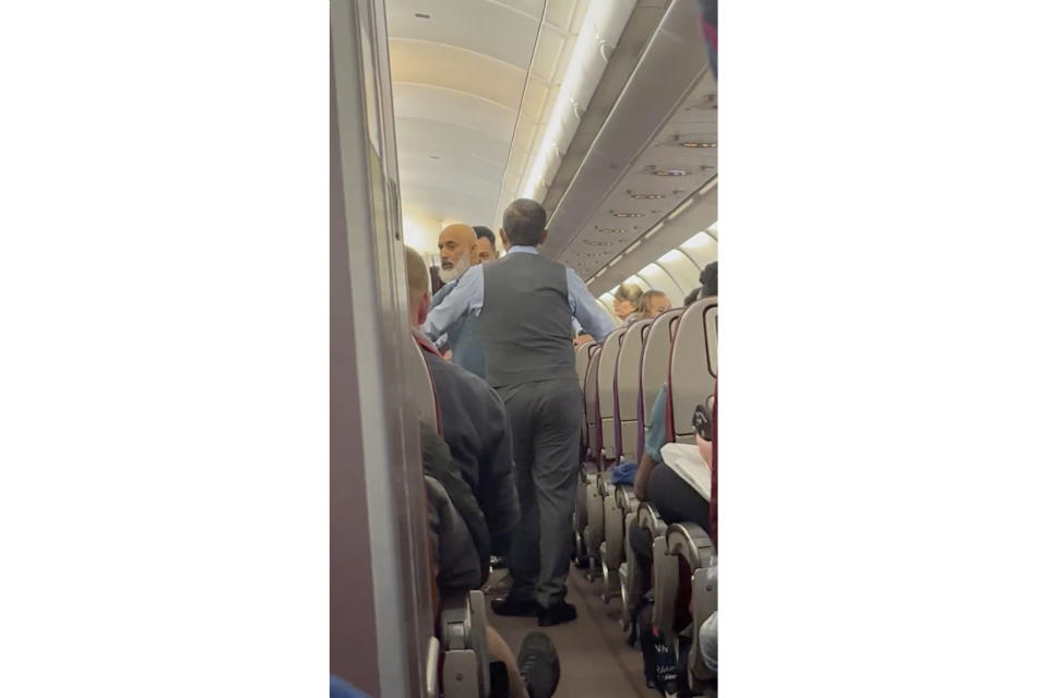 In this image from a video, a passenger, left, speaks with crew members during a flight from Australia to Malaysia, Monday, Aug. 14, 2023. Malaysia Airlines flight MH122 returned on Monday to Sydney, where the passenger was arrested hours later in what police described as an emergency incident. (Velutha Parambath via AP)